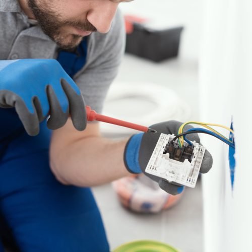 Professional electrician working on a home electrical system, he is installing a wall socket